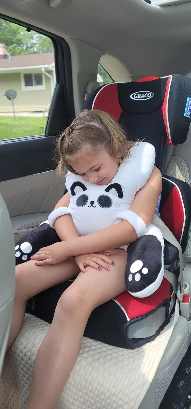 A girl asleep in her booster seat with Bao the Panda, a customer photo