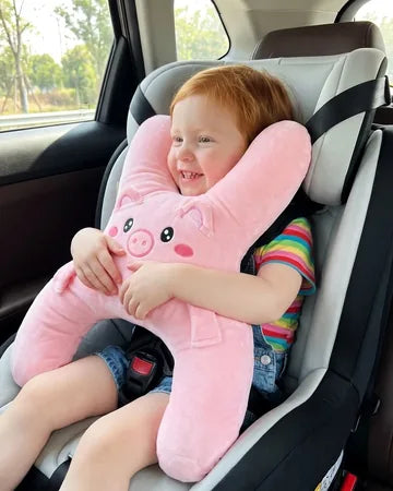A smiling toddler girl in a car seat hugging Ollie the Piggy